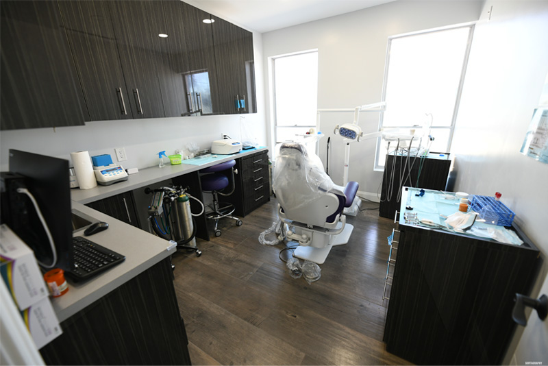 The image shows an interior of a dental office, featuring a clean and organized space with dental equipment, a chair for patient use, and a countertop with various items commonly found in such settings.