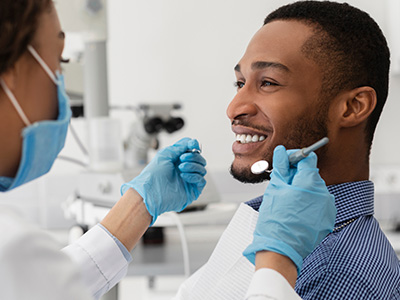 The image shows a man in a dental chair receiving dental care from a professional, with the focus on the man's smiling face and the dental equipment being used.