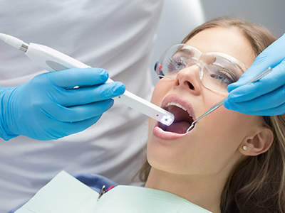 The image shows a dental hygiene professional performing a teeth cleaning procedure on a patient, with the use of specialized equipment and protective gear.