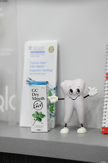 A dental clinic's counter with a toothbrush holder, a dental hygiene product, and a cartoon character of a toothbrush with arms raised.