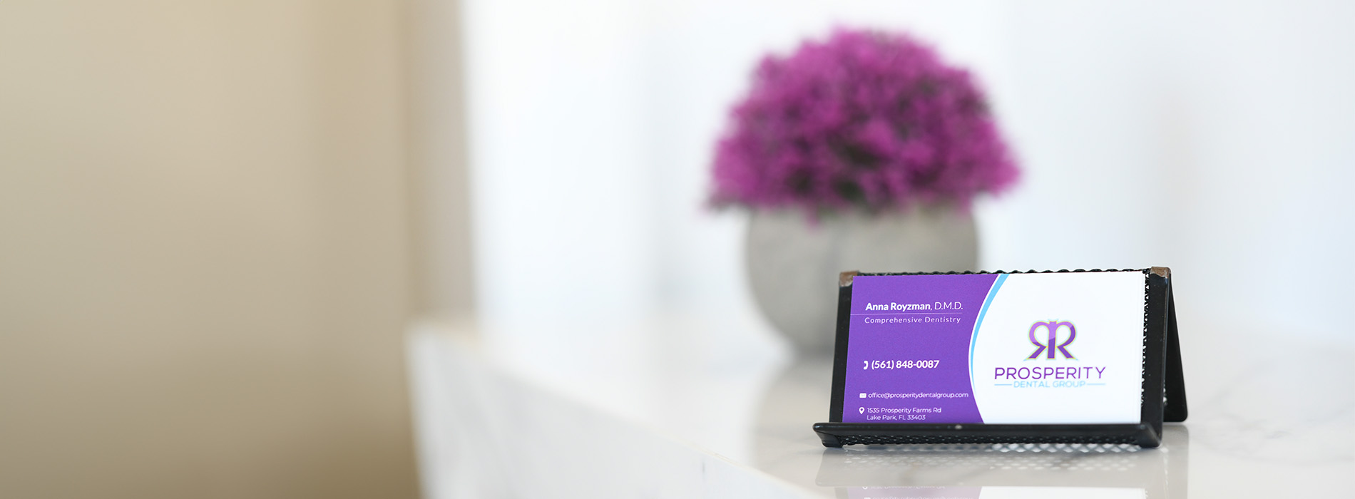 The image shows a white tablet with a purple screen displaying the text 'RKT', placed on a table in front of a blurred background that includes a vase and a plant.