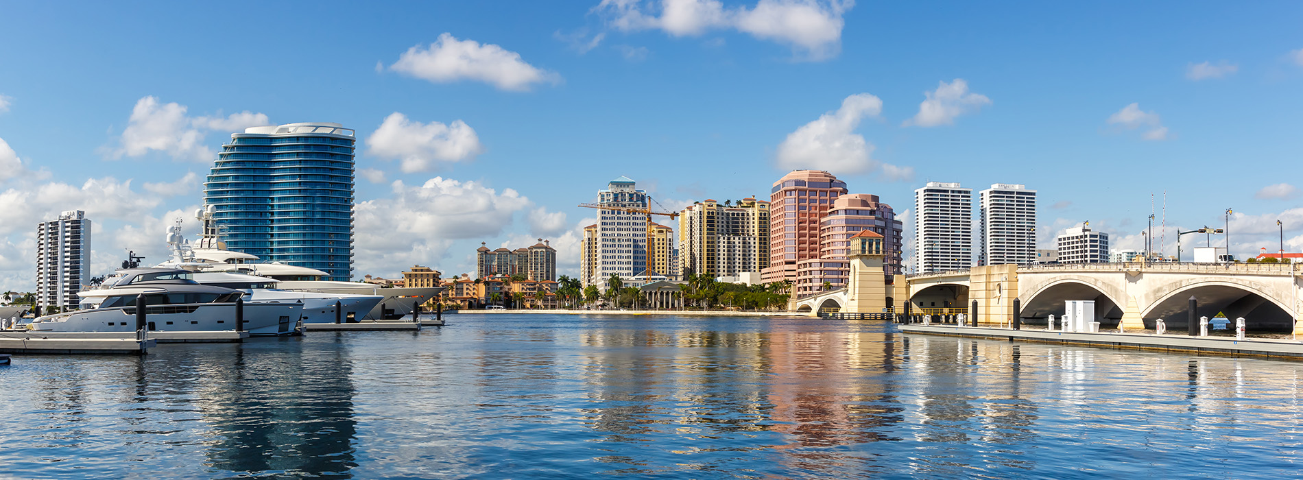 The image shows a city skyline with a river and boats, viewed from across the water.