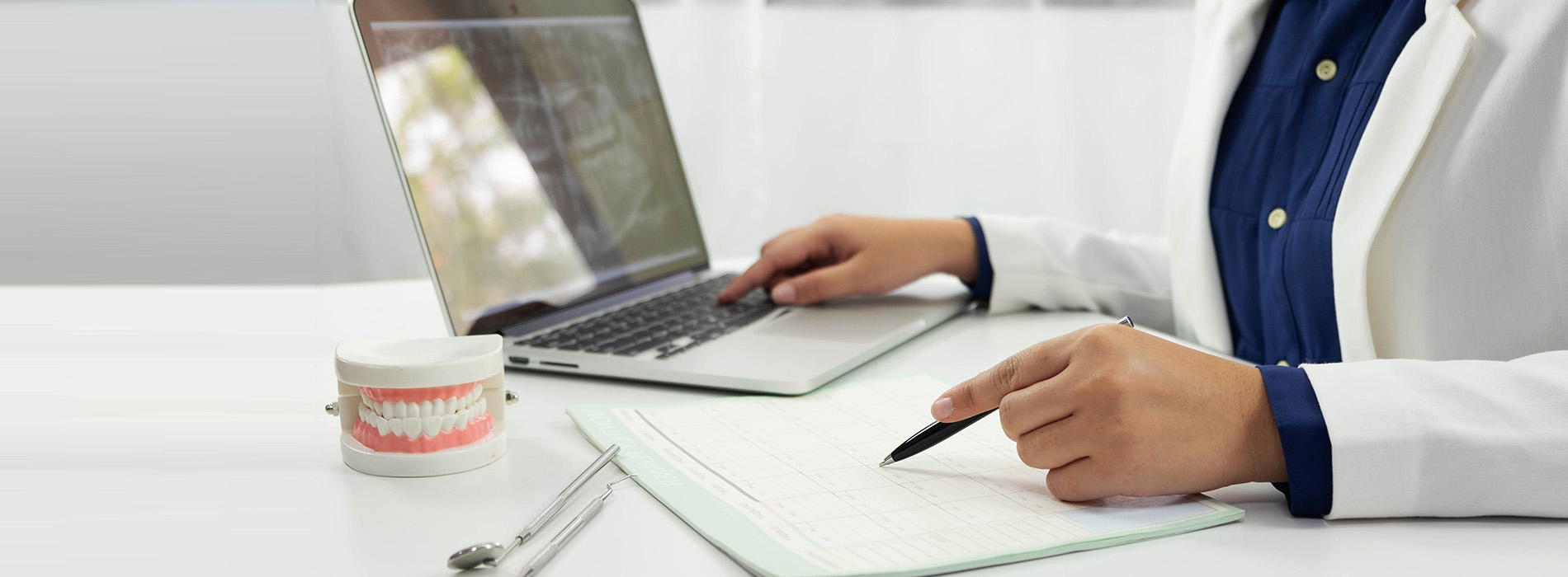 A person in a lab coat working at a desk with a laptop, papers, and a cup of coffee.