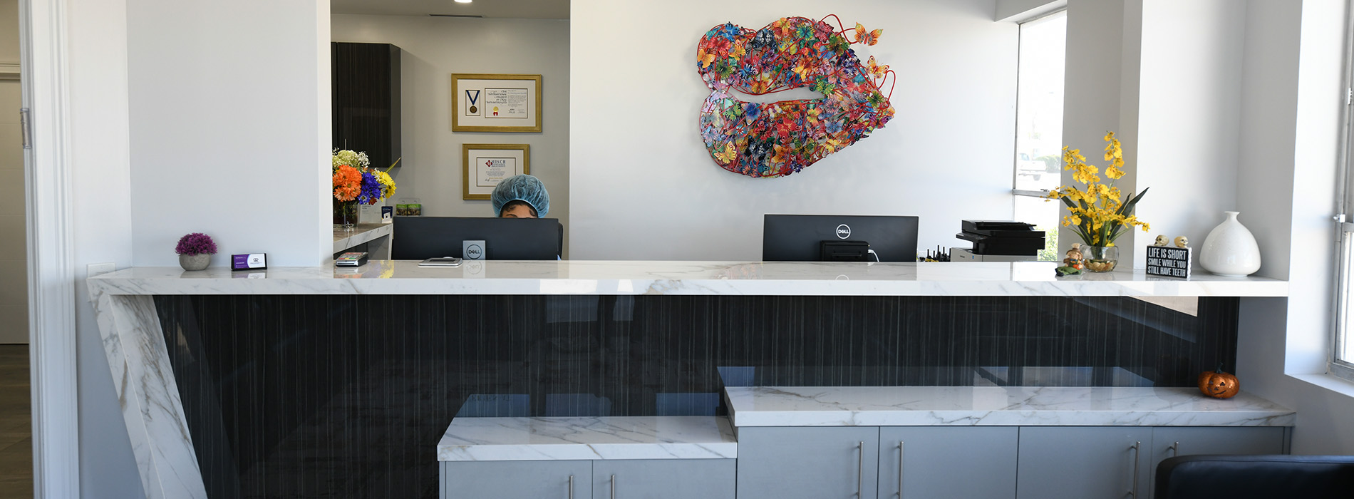 A modern interior space featuring a long, dark-toned countertop with a white backsplash, and a large, colorful abstract sculpture on the wall.