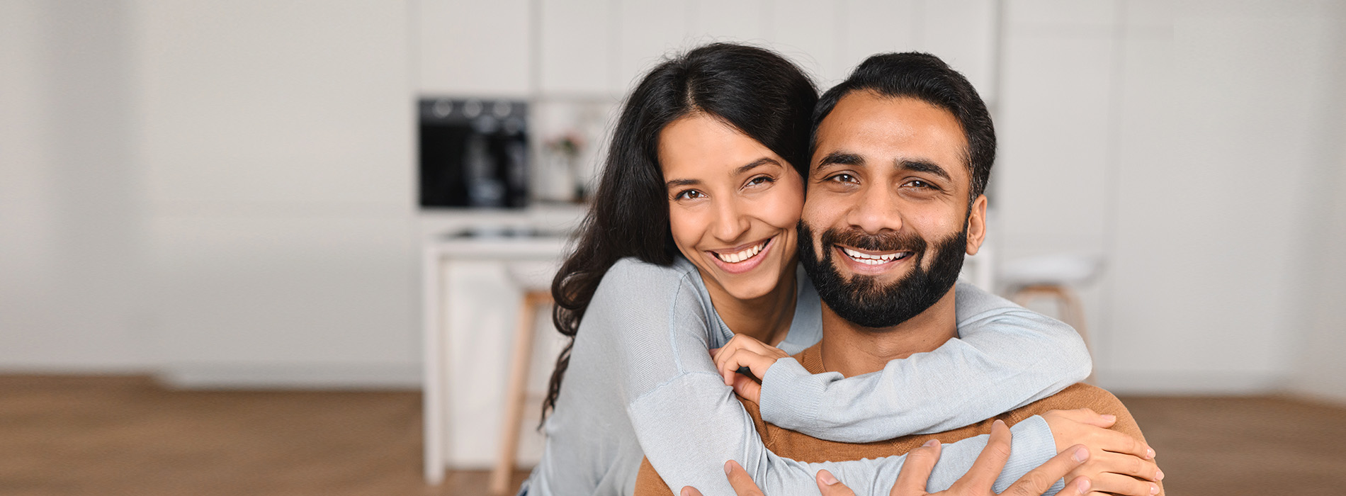 The image depicts a man and a woman in a warm embrace, smiling at the camera.