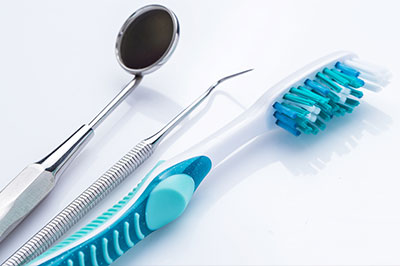The image shows a collection of dental tools, including a pair of blue toothbrushes and metal instruments, arranged on a white background.