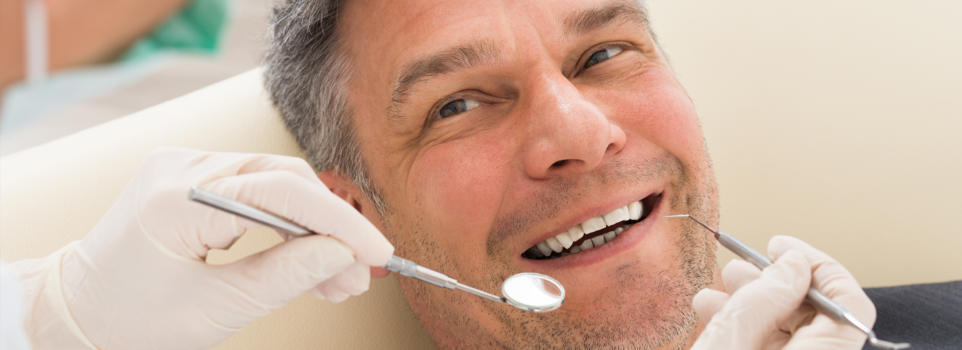 Man sitting in dental chair with smiling face, receiving dental treatment.