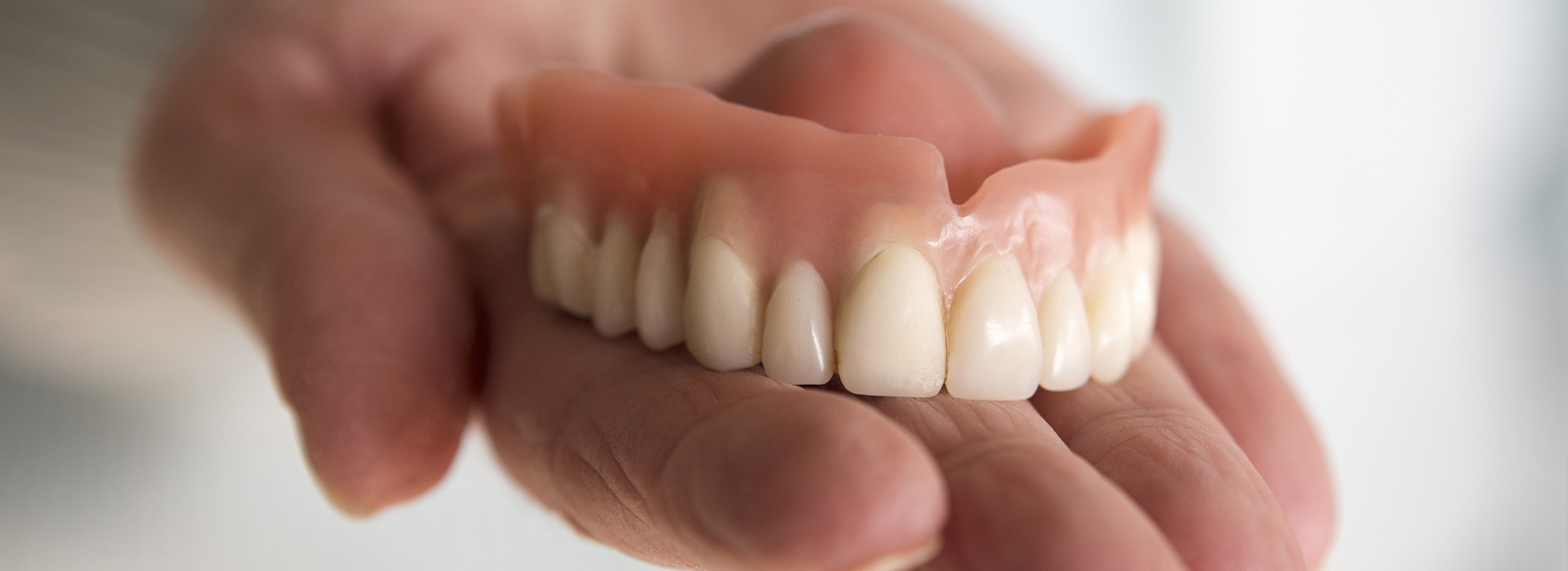 An image of a person's hand holding a set of dentures, with the dentures prominently displayed against a neutral background.