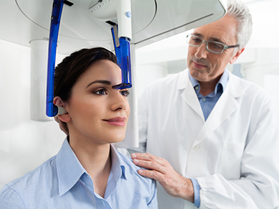 The image shows a woman seated in front of a 3D scanner, with a medical professional standing behind her, likely demonstrating or explaining the use of the device.