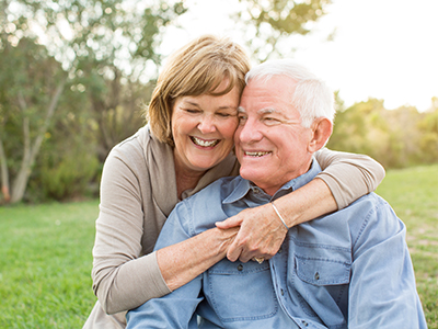 A man and a woman are embracing each other in a park setting, with the woman wearing a white top and the man dressed in blue.