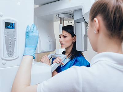 A woman in a blue uniform using a large white and gray 3D scanner, with another person observing the process.