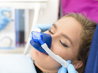 A person receiving dental care with a blue apparatus over their mouth, being attended to by a healthcare professional in a clinical setting.
